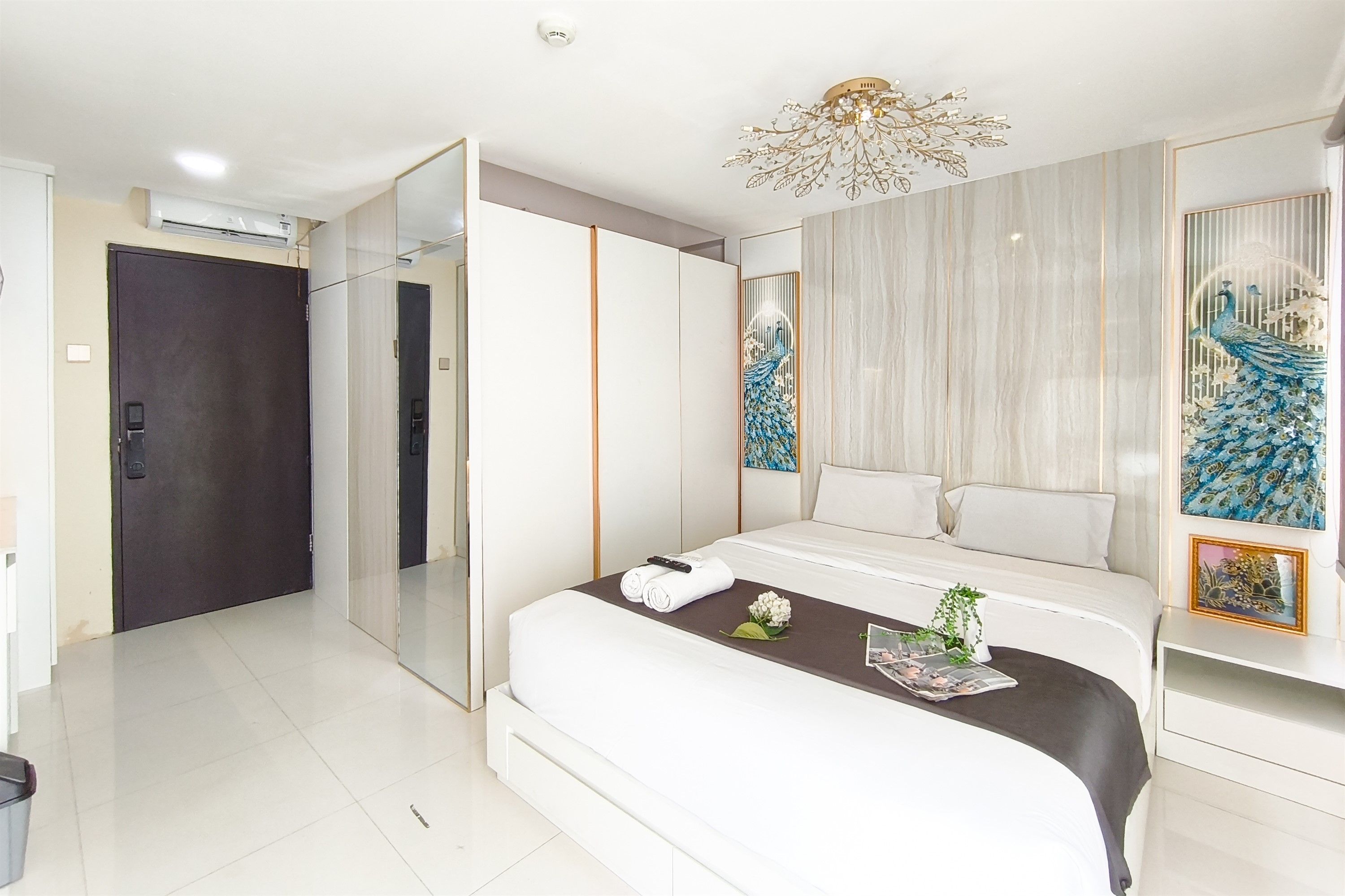 A modern hotel room with a large bed, a bedside table, a decorative peacock painting, and a ceiling light fixture.