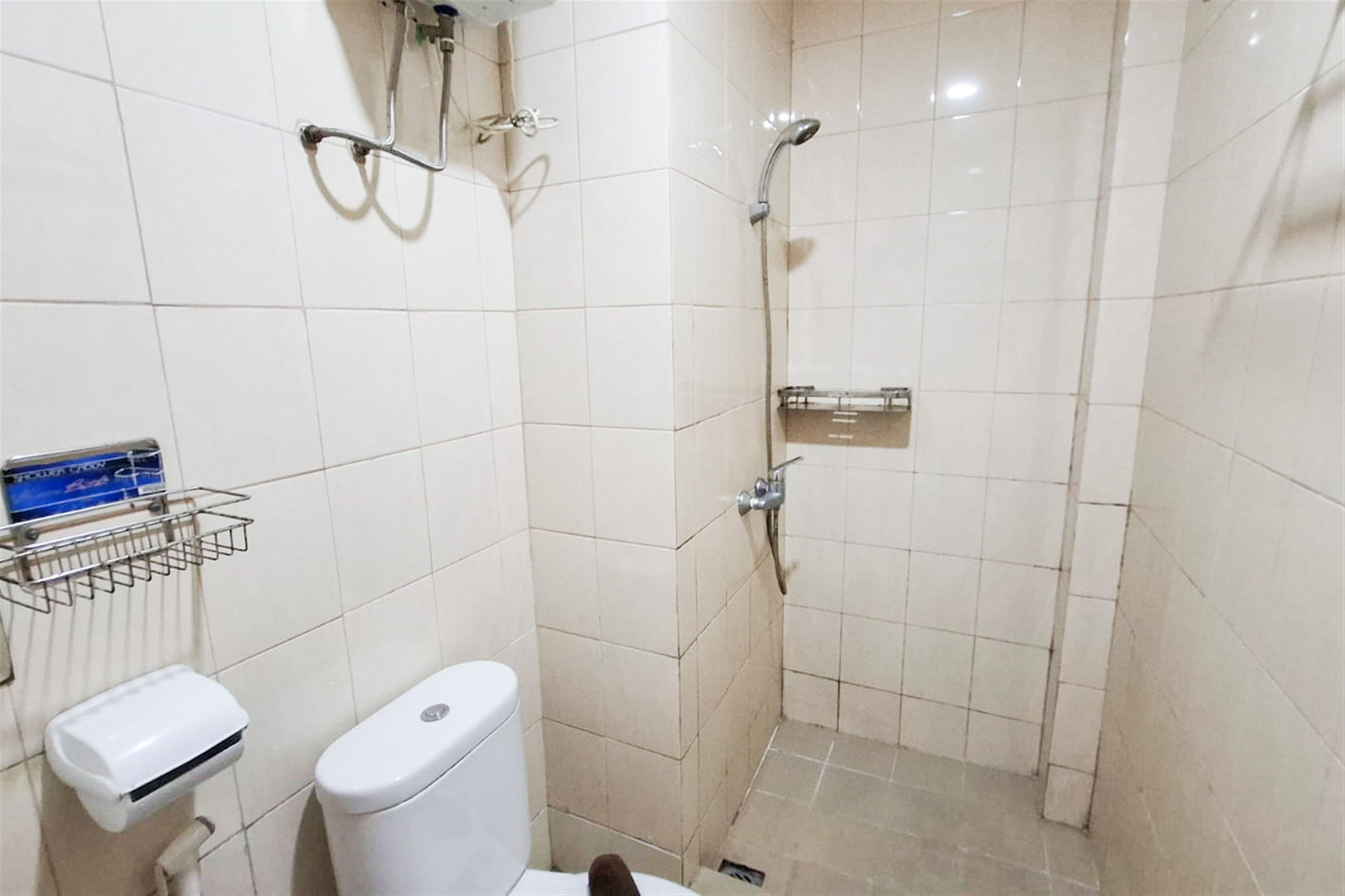 A small, tiled bathroom with a toilet, a hand dryer, and a shower area.