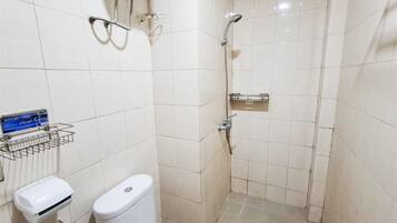 A small, tiled bathroom with a toilet, a hand dryer, and a shower area.