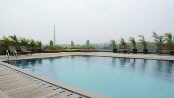 A rectangular swimming pool with a wooden deck surrounding it, benches, and potted plants.