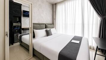 A modern hotel room with a bed, a desk, a wardrobe, and a television.