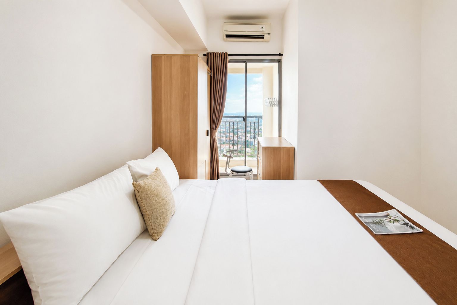 Habitación de hotel con cama, una mesita, una silla y vista de la ciudad desde una puerta de balcón.