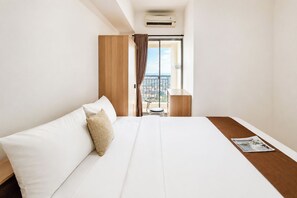 Habitación de hotel con cama, una mesita, una silla y vista de la ciudad desde una puerta de balcón.