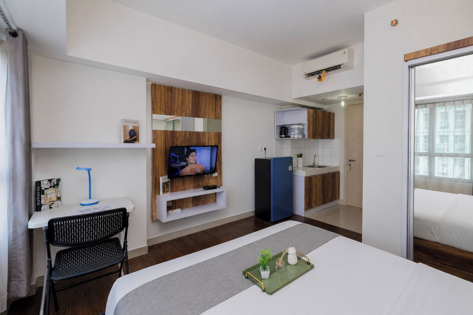 A hotel room with a bed, a desk with a chair, a television, a kitchenette, and a bathroom.