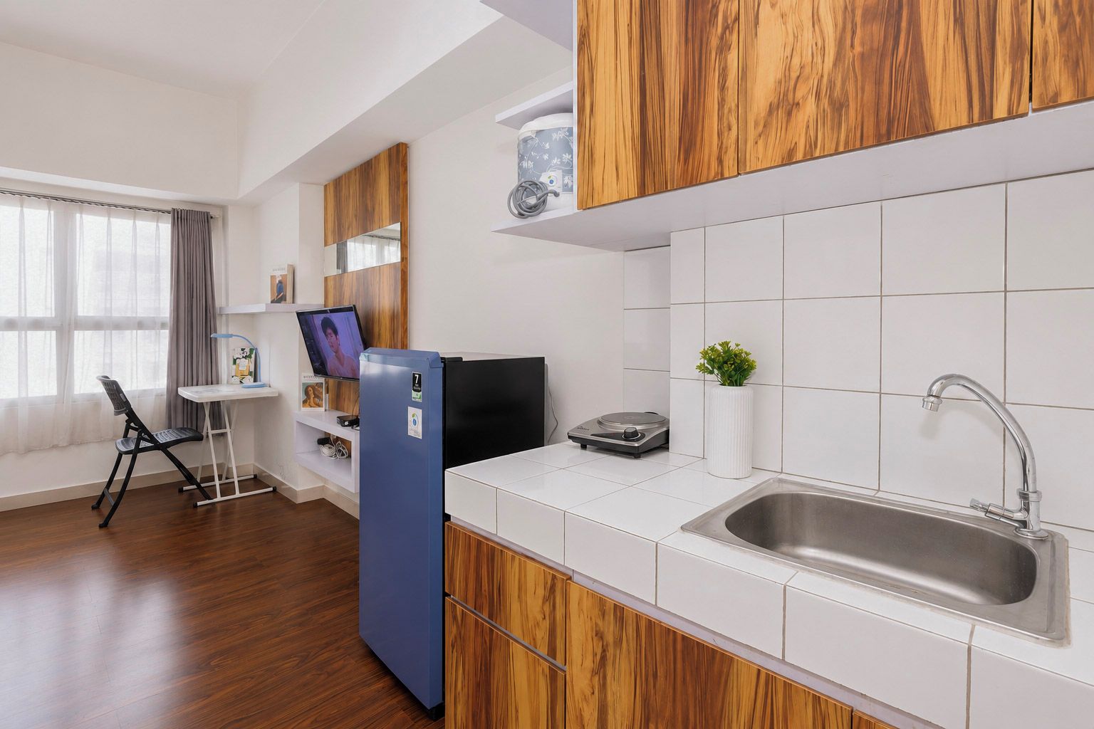 A modern kitchen with white tiles, wooden cabinets, a stainless steel sink, and a blue refrigerator.