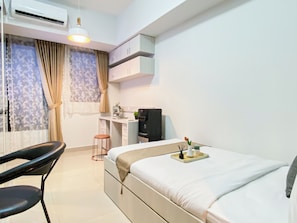 Ein Hotelzimmer mit einem Bett, einem Schreibtisch, einem Stuhl, einer Klimaanlage und einem fenster mit Vorhängen.
