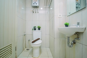 A small, compact bathroom with a toilet, a sink, and two potted plants. - Functional Homey Studio Room At Apartment Grand Kamala Lagoon (Bekasi)