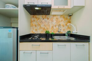A kitchen with a gas stove, a sink, and a refrigerator. - Functional Homey Studio Room At Apartment Grand Kamala Lagoon (Bekasi)