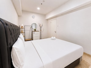 Ein Schlafzimmer mit einem Bett, einem Nachttisch, einer Lampe, einem Spiegel, einem Kleiderhaken und einer Tür.