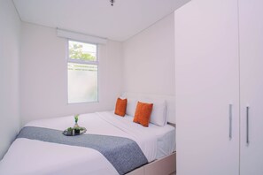 Ein Schlafzimmer mit einem Bett, Kissen, einem Nachttisch mit Pflanze und einem Fenster.