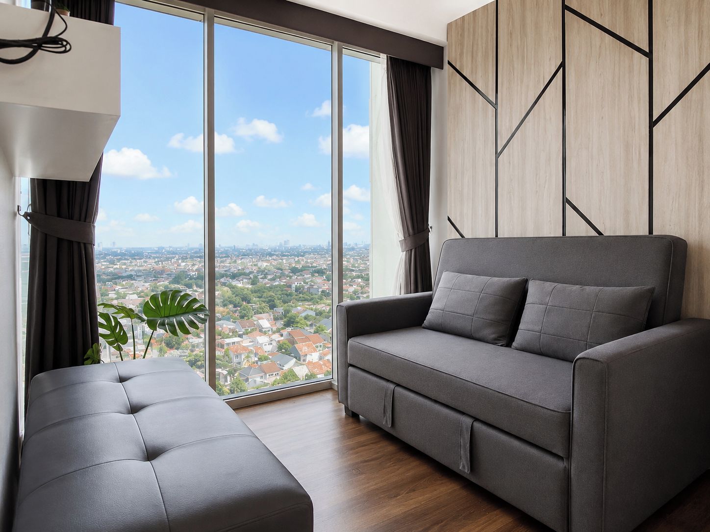 Uma sala de estar moderna com um sofá e um banquinho cinzas, grandes janelas com vista para a cidade e uma parede de destaque em madeira.