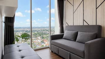 Uma sala de estar moderna com um sofá e um banquinho cinzas, grandes janelas com vista para a cidade e uma parede de destaque em madeira.
