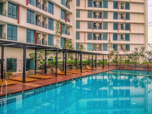Ein Pool mit Liegestühlen und einer überdachten Sitzgelegenheit, umgeben von einem mehrstöckigen Gebäude mit Balkonen.