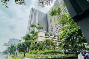 Un immeuble moderne de grande hauteur, dont la façade est un mélange de verre et de béton, entouré d’une végétation luxuriante et de palmiers.