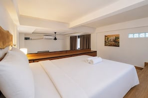 Ein Hotelzimmer mit einem großen Bett, einem Deckenventilator, einem Gemälde an der Wand und einem Fenster mit Vorhängen.