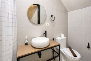 Ein modernes Badezimmer mit einem runden Spiegel, einem weißen Waschbecken und einer Toilette.