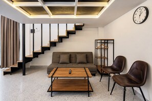 A modern living room with a sofa, two chairs, a coffee table, a wooden staircase, and a wall-mounted clock. - Loft Studio Villa Kerobokan Near Seminyak (Kerobokan)
