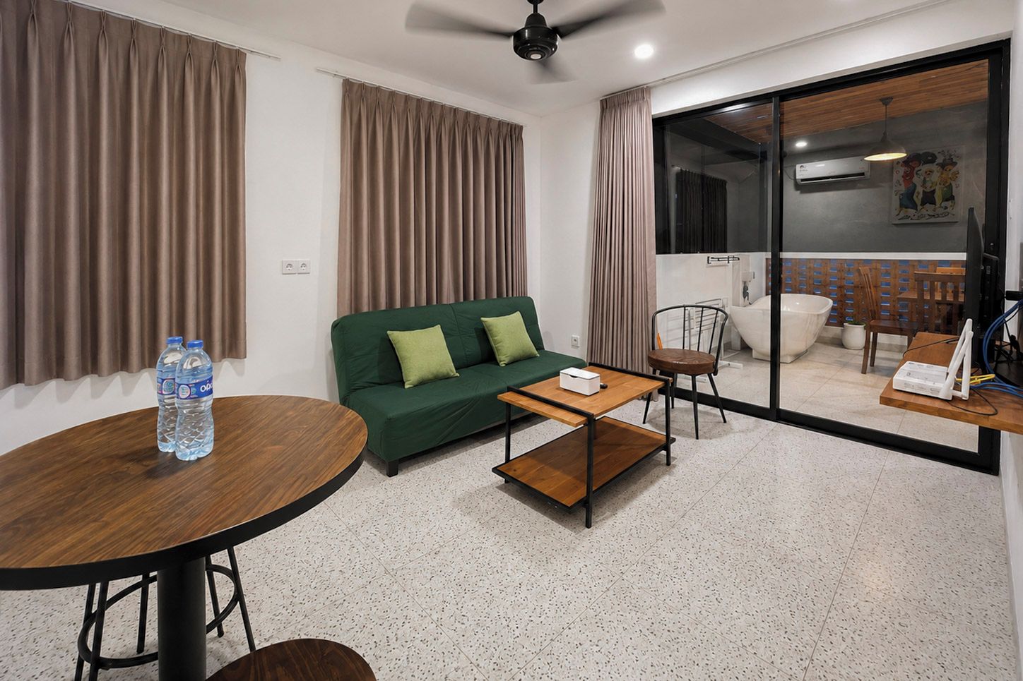 A modern living room with a green sofa, a round wooden table, and a glass sliding door leading to a balcony.