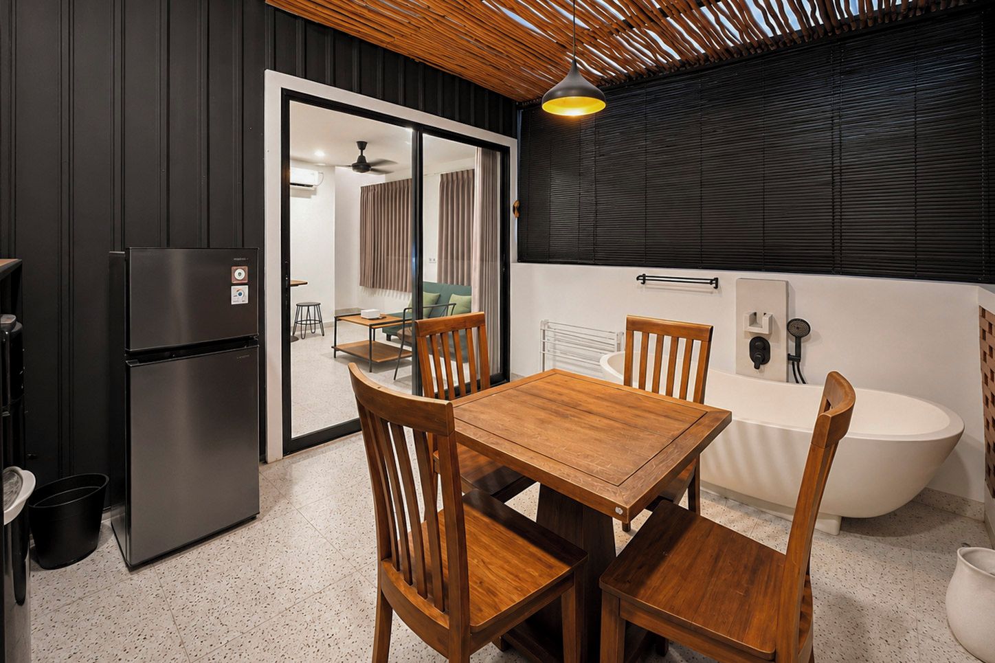 A compact kitchen with a refrigerator, wooden dining table, chairs, and a bathtub with a shower.