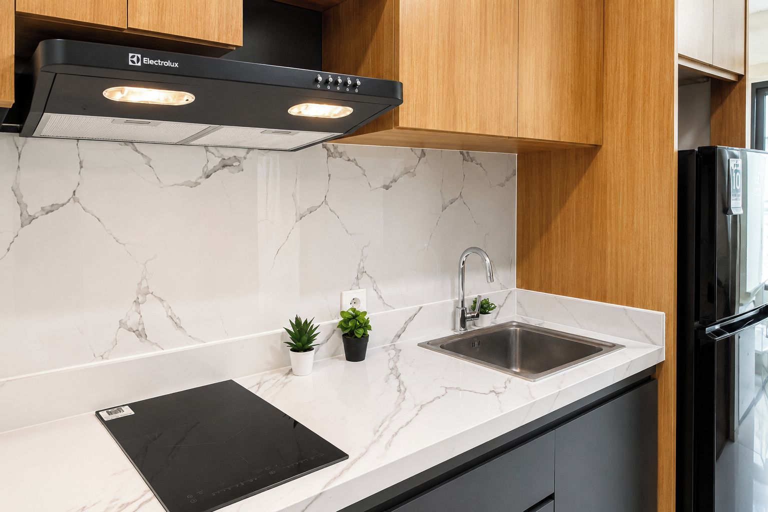 A modern kitchen with a black range hood, a stainless steel sink, and a black induction cooktop.
