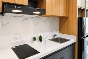 Una cocina moderna con un extractor de aire negro, un lavamanos de acero inoxidable y una placa de inducción negra.