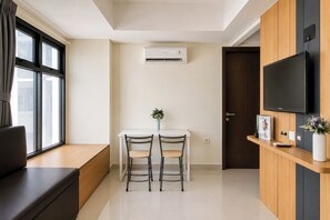 Una sala de estar moderna con un sofá, una mesa de comedor con dos sillas, un televisor montado en la pared y un aire acondicionado.