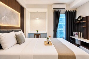 Quarto de hotel com cama, escrivaninha, janela com cortinas e ar condicionado.