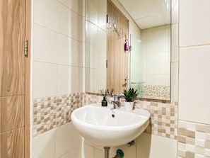Casa de banho com lavatório branco, espelho e painel de azulejos xadrez.