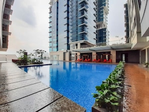 Piscina com deck de madeira, cercada por edifícios altos.