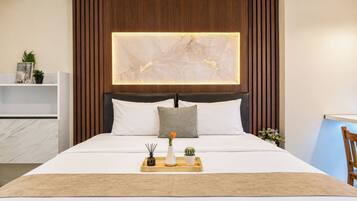 Una habitación de hotel con una cama, una mesita de noche con bandeja, una obra de arte en la pared y un cabecero de madera.