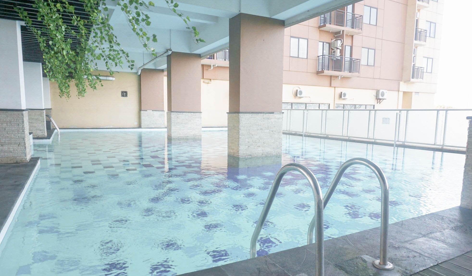 An indoor swimming pool with clear water, surrounded by a tiled floor and concrete pillars.
