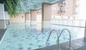 Une piscine intérieure à l’eau claire, entourée d’un sol carrelé et de piliers en béton.