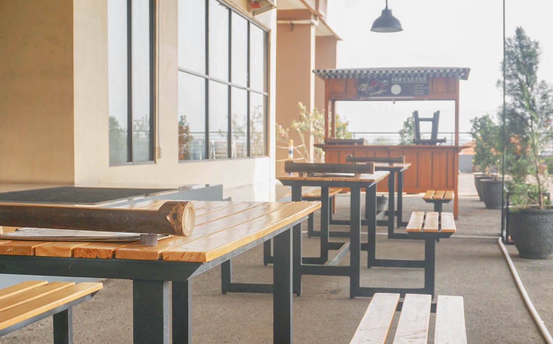 An outdoor seating area with wooden tables and benches, a view of the building's exterior, and a sign above the entrance.