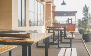 Un espace extérieur aménagé avec des tables et des bancs en bois, une vue sur la façade du bâtiment et une enseigne au-dessus de l’entrée.