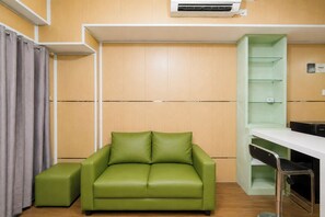 A room with a green sofa, a small ottoman, a white desk, and a green shelving unit. - Contemporary 2Br At Apartment Tamansari Panoramic (Bandung)