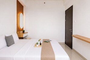 A hotel room with a bed, bedside table, mirror, and a door. - Bright And Relaxing 1Br At Apartment Lrt City Bekasi (Bekasi)