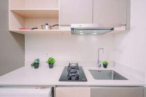 A kitchen with a stainless steel range hood, a double sink, and three potted plants on the countertop. - Refined And Airy Studio At Apartment Gold Coast (Jakarta)