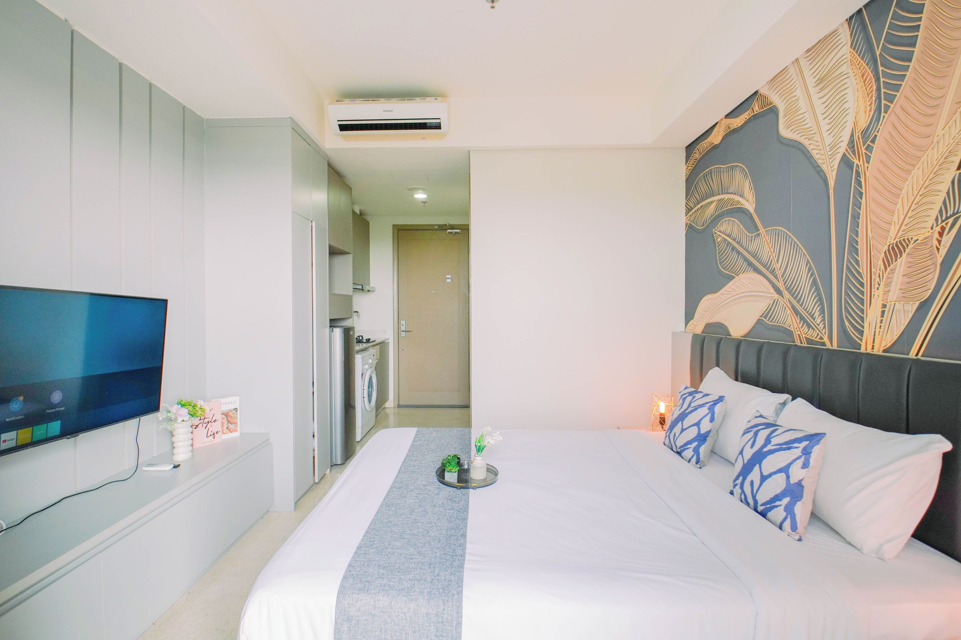 A hotel room with a bed, a television, a washing machine, and a decorative wall.