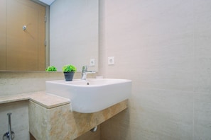 A bathroom with a white sink, a mirror, and a potted plant. - Refined And Airy Studio At Apartment Gold Coast (Jakarta)