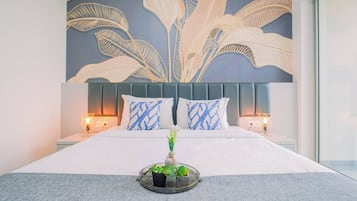 A hotel room with a large bed, two bedside lamps, a decorative wall mural, and a bedside plant.