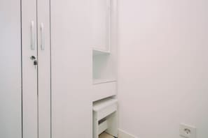 Quarto branco com porta, termostato e estante.