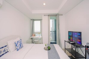 A hotel room with a bed, a desk, a TV, and a balcony with a view. - Bright Elegant Studio At Apartment Antasari Place (Jakarta)