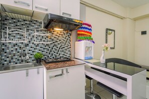 Een moderne keuken met een gasfornuis, een magnetron en een koffieapparaat. Op het aanrecht staat een klein plantje en boven het fornuis hangt een kleurrijk gehaakt object.