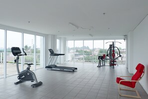 Ein geräumiger Fitnessraum mit Cardiogeräten, einem roten Stuhl und Blick auf die Stadt durch große Fenster.