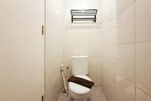 A small, tiled bathroom with a white toilet, a towel rack above the toilet, and a toilet paper holder on the wall. - Attractive And Stylish Studio At Apartment Poris 88 (Tangerang)