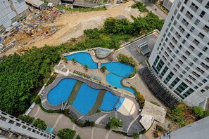 An aerial view of a residential area with a swimming pool complex surrounded by greenery and adjacent to a construction site. - Roomy Good Location 2Br At Apartment The Wave Kuningan (Jakarta)