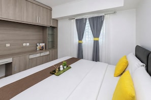 A hotel room with a bed, bedside table, and a desk area with a chair. - Roomy Good Location 2Br At Apartment The Wave Kuningan (Jakarta)