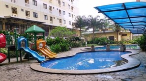 A swimming pool with a slide, surrounded by a paved area and a building with balconies. - Tranquil And Modern Studio At Apartment Kebagusan City (Jakarta)