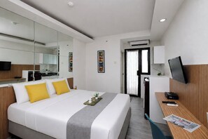 A modern hotel room with a large bed, a desk with a flat-screen TV, a mirror, and a door leading to a bathroom. - Tranquil And Modern Studio At Apartment Kebagusan City (Jakarta)