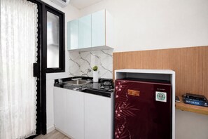 Eine kompakte Küche mit schwarzem Arbeitsplatz, weißen Schränken, einer Marmor-Spritzschutzleiste und einem roten Kühlschrank mit Aufkleber.